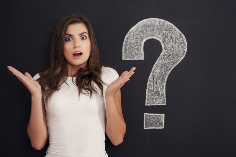 A confused girl beside a big question mark in a black wall.