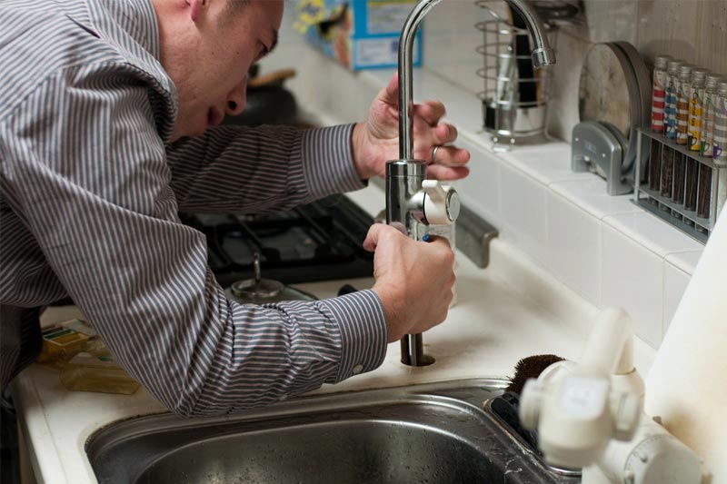 A man in a stripe sleeve installing a faucet in the sink.