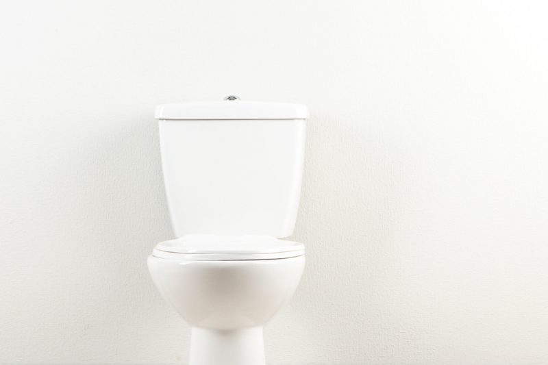 Toilet in front of white wall.